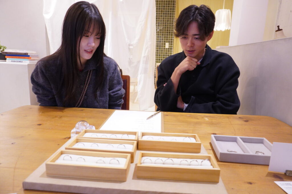 槌目デザインの結婚指輪サンプルを見ながら悩むカップルの様子